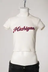 Remera baby tee blanca de morley, con ajuste al cuerpo, mangas cortas, cuello redondo y estampado con la inscripción 'Michigan' en estilo college.