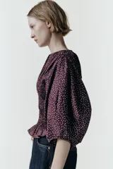 Blusa de color bordó con estampado de lunares claros, confeccionada con cuerpo en nido de abeja elástico, cuello redondo y mangas abullonadas por debajo del codo.
