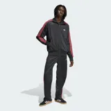 Campera deportiva Adidas modelo Firebird Loose Pinstripes, de color negro con diseño de rayas diplomáticas sutiles. Cuenta con cuello alto, cierre frontal completo, bolsillos laterales y bandas tricolor en rojo, blanco y negro a lo largo de las mangas. Incluye el logo del trifolio bordado en el pecho.