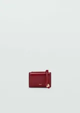 Monedero de efecto piel color rojo burdeos, con tamaño pequeño, cierre de solapa con botón magnético, bolsillo lateral con cremallera y detalle de abalorio colgante.
