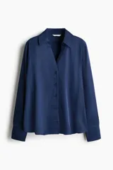 Blusa de tela satinada con brillo, cuello clásico, escote en V con cierre frontal de botones, mangas largas con puños sencillos y bajo redondeado.