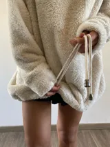Hoodie oversize de textura tipo peluche, color beige, con capucha ajustable mediante cordones y ajuste en el ruedo inferior.