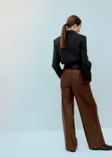 Pantalón de corte wide leg, confeccionado en material sintético efecto cuero color marrón, con pinzas en la cintura y bolsillos laterales.