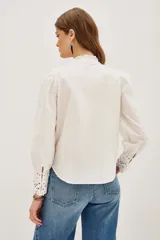 Camisa negra de algodón con detalles de encaje calado en el pecho, hombros y puños. Presenta cuello alto con terminación de encaje, cierre frontal con botones y mangas largas abullonadas.