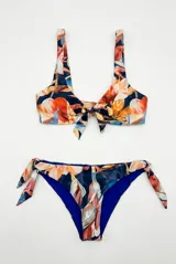 Conjunto de bikini con estampado floral en tonos azules, naranjas y blancos, compuesto por un top con nudo frontal y tirantes anchos, y una bombacha vedetina ajustable con lazos en los laterales.