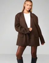 Blazer oversized color marrón chocolate con diseño de rayas finas verticales (pinstripe). Presenta solapas clásicas, cierre frontal con botones y bolsillos delanteros con solapa.