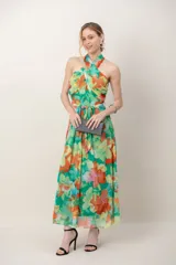 Vestido largo de gasa estampado con diseño floral en tonos verdes, naranjas y amarillos. Cuenta con escote halter cruzado, tiras para atar en la cintura y falda fluida al tobillo.