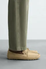 Mocasín casual de cuero color marrón claro con acabado serraje, horma redonda, detalle de lazo en el empeine y suela de goma.