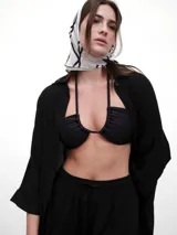 Top de bikini negro, estilo bandeau, con frunce central y abertura en el escote. Posee breteles finos que se anudan al cuello en forma cruzada.