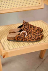 Zueco de mujer con estampado animal print tipo leopardo, diseño cerrado en la parte delantera y tira lateral con hebilla decorada con perlas sintéticas. Cuenta con suela de corcho y base plana.
