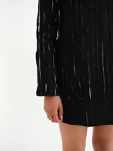 Vestido corto negro con textura de rayas verticales claras, escote redondo y mangas largas.
