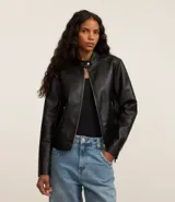 Campera negra de cuero sintético con cuello mao, cierre frontal asimétrico y bolsillos con cremallera.