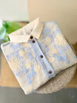 Camisa de manga corta color natural con delicados bordados florales en celeste y crema, transparencias, cuello clásico y botones frontales.