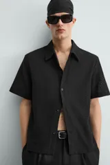 Camisa regular fit de manga corta confeccionada en tejido jacquard con estructura abierta y diseño geométrico. Presenta cuello solapa y cierre frontal con botones al tono.