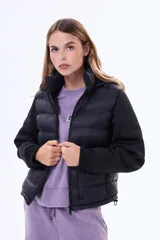 Campera negra de estilo híbrido, con cuerpo acolchado y mangas de tejido liso. Presenta cuello alto, cierre frontal y puños elásticos.
