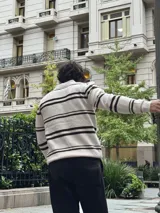 Buzo tejido de punto con diseño a rayas horizontales en color beige y marrón. Presenta cuello tipo polo con cierre frontal parcial y puños acanalados.