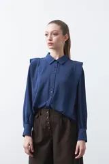 Camisa negra de estilo sastrero con cuello clásico, frente abotonado y mangas largas con puños ajustados. Presenta un diseño con hombreras sutiles que aportan estructura a la prenda.