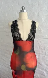 Vestido midi de microtul rojo con estampado de rosas y hojas verdes, escote en V con encaje negro y breteles finos regulables en la espalda.