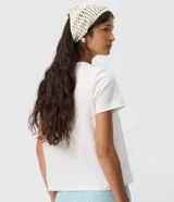 Remera de algodón blanca, de manga corta y cuello redondo, con estampa frontal inspirada en paisajes tropicales y detalles de lentejuelas.