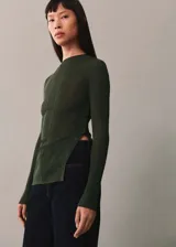 Buzo de punto fino en color verde oscuro, con cuello perkins y manga larga. Presenta un diseño semitransparente con una abertura lateral decorada con una hilera de botones a tono.