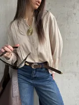 Camisa beige de manga larga con detalles de vainica vertical en el frente y cierre frontal de botones.