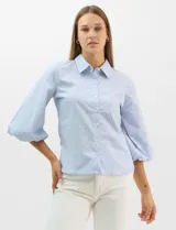 Camisa de algodón con patrón de rayas verticales, cuello camisero clásico y cierre frontal con botones. Presenta detalles metálicos aplicados en el frente y mangas, con mangas 3/4 abullonadas y ruedo recto.