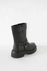 Bota de caña media confeccionada en cuero negro, con suela gruesa track antideslizante. Presenta un diseño estilo biker con estribo integrado, hebillas metálicas decorativas y una correa ajustable en la parte superior de la caña. Incluye cierre lateral para facilitar el calce.