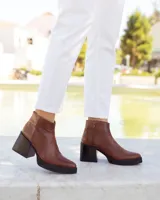 Botines de cuero marrón, hechos a mano en Uruguay, con plataforma delantera y taco ancho y alto de color negro. Presentan un detalle de textura de piel de reptil en la parte superior del talón y cierre lateral con cremallera.