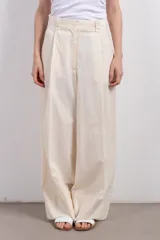 Pantalón de vestir color crema, de tiro medio y corte ancho. Presenta pinzas en la parte delantera y largo hasta los tobillos.