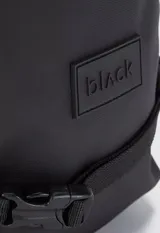 Mochila tipo bandolera de un solo hombro, color tostado, con correas ajustables negras y cierre frontal.