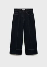 Pantalón de jean estilo wide leg con tiro medio y diseño crop. Presenta costuras verticales decorativas en el frente, cinco bolsillos, trabillas para cinturón y cierre frontal con cremallera y botón.