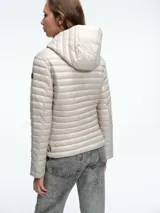 Campera acolchada ultraligera de color blanco, con capucha, cierre frontal de cremallera y bolsillos laterales. Diseño entallado con acabado resistente al viento y la humedad.