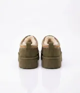 Zueco de gamuza color tostado con interior forrado en piel sintética. Presenta una banda decorativa bordada con motivos étnicos en el borde superior y una suela de plataforma plana de goma.