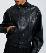 Campera estilo bomber de cuero sintético (PU) color negro, con cuello alto estructurado, cierre frontal con cremallera y botones a presión, mangas largas y detalle de cinturón ajustable en la cintura.