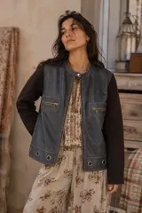 Campera bicolor con frente de cuero sintético gris oscuro y mangas y espalda de tejido marrón. Presenta cuello mao con broche a presión, cierre frontal y bolsillos con cierre en el pecho. El ruedo está decorado con ojalillos metálicos aplicados.