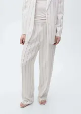 Pantalon de vestir de corte wide leg, color beige con estampado de rayas verticales finas en tono oscuro. Presenta tiro medio, cierre frontal con botón y cremallera, trabillas para cinturón y bolsillos laterales.