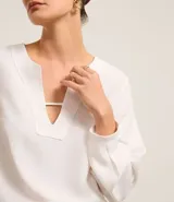 Blusa blanca de crepé con cuello en V, mangas largas y pliegues en los puños.