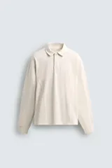 Polo de manga larga color crema, confeccionado en tejido de algodón, con cuello solapa y cierre frontal de botonadura. Presenta un calce relajado y acabados en rib en puños y ruedo.