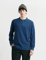 Remera de punto canalé francés azul, con cuello polo, manga larga y cierre metálico corto en el frente.