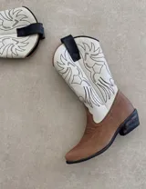 Botas de cuero color marrón y blanco con bordados negros, de estilo cowboy con taco bajo.