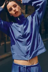 Chaqueta azul de algodón con cuello alto, cierre frontal de cremallera, bolsillos laterales y mangas largas con puños elásticos.