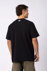 Remera de corte oversized en color marrón, confeccionada en tejido de algodón con textura de micropanal. Presenta cuello redondo con detalle de costura en forma de X y mangas cortas de estilo caído.