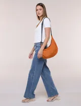 Cartera bandolera de lona naranja en forma de medialuna, con correa ajustable negra y cierre principal.