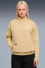 Buzo Puma Ess Script Half Zip Crew color tostado, con cuello alto, cierre frontal parcial, bolsillo tipo canguro y logo bordado en el pecho.