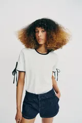 Camiseta de algodón de corte regular, color blanco con detalles de vivos y lazos en contraste negro en el cuello y en las mangas cortas.