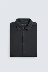 Camisa de corte relajado confeccionada en tejido de algodón con textura. Presenta cuello italiano, manga larga con puños abotonados y cierre frontal mediante botonadura.