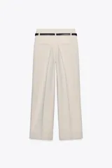 Pantalón de vestir color beige, tiro alto, corte ancho y pierna recta. Presenta un bajo con vuelta y viene acompañado de un cinturón fino de cuero marrón con hebilla metálica.