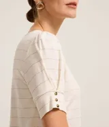 Blusa de viscosa texturizada color beige, con rayas horizontales en hilo metalizado, cuello redondo y mangas cortas con botones.