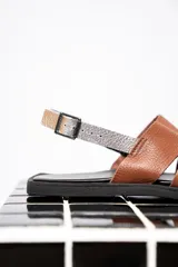 Sandalias chatas color marrón con tiras anchas de cuero y pulsera al tobillo con hebilla metálica.