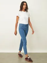 Jean de corte skinny en color azul medio, con tiro medio, cierre frontal con botón y bolsillos laterales y traseros.